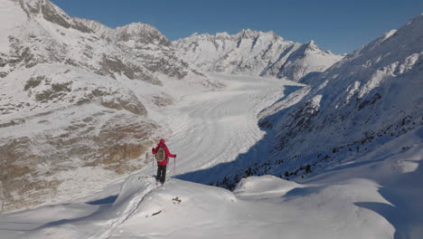 Luftaufnahme-In-Der-Schweiz-Mit-Einer-Person,-Die-An-Einem-Sonnigen-Tag-Mit-Einem-Gletscher-Dahinter-Mit-Schneeschuhen-Geht