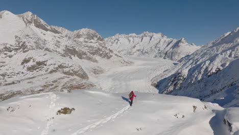 Luftaufnahme-In-Der-Schweiz-Mit-Einer-Person,-Die-An-Einem-Sonnigen-Tag-Mit-Einem-Gletscher-Dahinter-Mit-Schneeschuhen-Geht