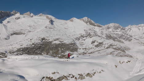 Aerial-shot-in-Switzerland-with-a-person-walking-with-snow-shoes-on-a-sunny-day-with-a-glacier-behind