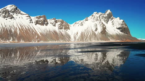 A-Man-Standing-In-Front-Of-Vestrahorn-Mountain-With-Perfect-Reflection-At-Daytime-In-South-Iceland