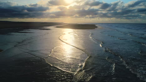 Stunning-Beautiful-Low-Aerial-Drone-Shot-Over-Small-Waves-Breaking-on-Sandy-Beach-at-Golden-Hour-Sunset-UK