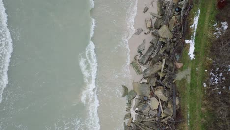 Aerial-birdseye-view-of-Baltic-sea-coast-on-a-overcast-winter-day,-concrete-blocks-on-the-beach-with-white-sand,-coastal-erosion,-climate-changes,-wide-drone-shot-moving-forward