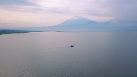 Drone-shot-of-a-boat-on-the-middle-of-huge-lake-with-mountain-on-the-background---Rawa-Pening-Lake,-Indonesia