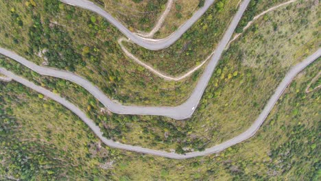 Cars-and-trucks-traveling-on-zigzag-switchback-countryside-rural-roads,-directly-above-descending-aerial