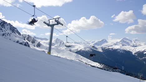 Skiers-ride-ski-lift-with-snowy-mountain-background,-Whistler,-Canada