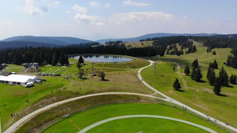 Trails-in-Rogla-sports-resort-Slovenia-during-springtime-passing-around-a-small-lake-near-a-soccer-field,-Aerial-flyover-shot