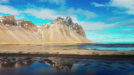 Man-Running-Facing-Towards-Vestrahorn-Mountain-In-South-Iceland-On-A-Cloudy-Blue-Sky---Drone-Shot