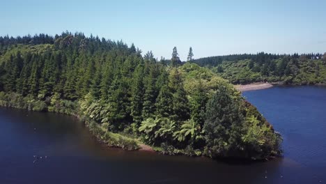 Drone-shot,-rotating-angle-of-an-island-full-of-trees-in-the-middle-of-a-lake-in-New-Plymouth