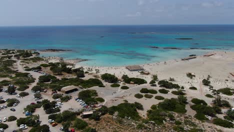 Elafonissi-Beach-in-Crete-Greece-with-parking-lot-and-guest-area-with-vehicles,-Aerial-dolly-out-reveal-shot