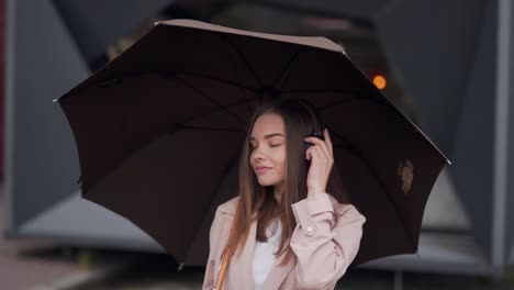 Modisches-Hübsches-Mädchen-Hört-Musik-über-Kopfhörer-Mit-Einem-Regenschirm-Auf-Dunklem-Hintergrund