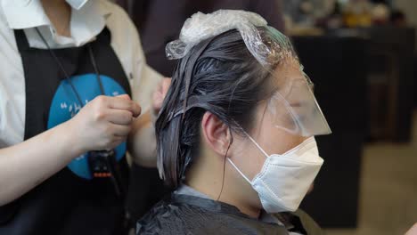 Korean-woman-wearing-face-mask-and-eye-protection-has-hair-pulled-by-stylists-inside-salon,-close-up