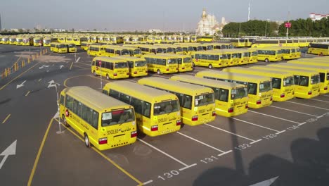 Yellow-school-buses-in-parking-lot,-rear-aerial-shot