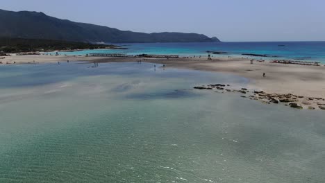 Ocean-lagoon-at-Elafonissi-Beach-in-Crete-Greece-with-bathers-on-the-shore,-Aerial-dolly-out-shot