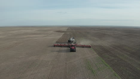 A-Seeder-Tractor-Seeding-At-The-Farmland-In-Swift-Current,-Saskatchewan,-Canada---ascending-drone-shot