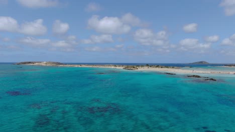 Playa-Turquesa-De-Elafonissi-En-Creta-Grecia-Con-Aguas-Poco-Profundas-Transparentes-Y-Arrecifes-De-Roca,-Tiro-Aéreo