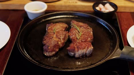 Two-beefsteak-sirloin-pieces-on-meat-fried-on-frying-pan-in-Korean-restaurant-Static