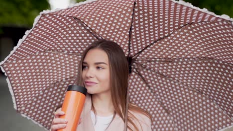 Schönes-Mädchen-Trinkt-Ein-Getränk-Aus-Einer-Thermoskanne,-Die-Einen-Regenschirm-Hält
