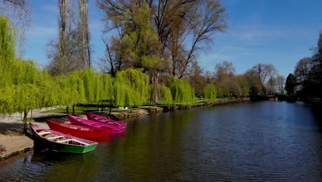 Paradise-tranquil-park-with-anchored-boats-on-bank-of-canal-under-green-willows-on-a-sunny-spring-day