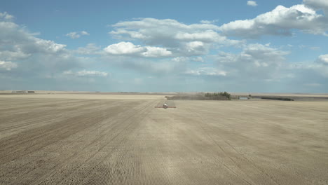 Spectacular-aerial-flyover-of-industrial-tractor-seeding-rows-of-farm-land-in-vast-rural-flat-plains-countryside-on-beautiful-blue-sky-day,-Swift-Current,-Saskatchewan,-Canada,-drone-approach