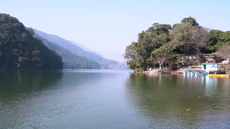 Toma-Panorámica-Lenta-Del-Lago-Fewa-Ubicado-En-Pokhara,-Nepal,-Con-Los-Barcos-Estacionados-Cerca-De-La-Orilla