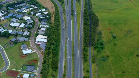 Vehicles-Driving-At-Carriageway-Of-Pacific-Motorway-Near-Typical-Houses-On-Lush-Fields-Connecting-Byron-Bay-And-Brisbane,-Queensland,-Australia