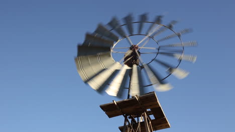 low-angle-view-of-an-agricultural-wind-pump-turning-against-a-vibrant-and-clear-blue-sky