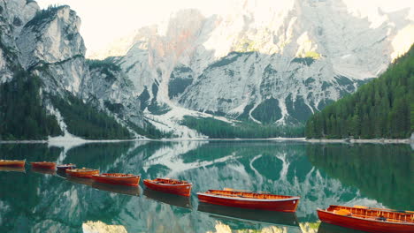 Stunning-reflections-of-the-Prags-Dolomites-and-a-line-of-red-wooden-rowboats-in-Lake-Braies,-Italy,-aerial