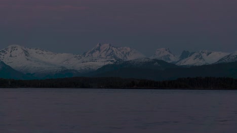Time-lapse-of-beautiful-scenery-of-mountains-covered-with-snow-during-sunset,-ocean-in-foreground,-frame-zooming-out