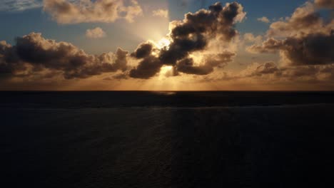 Beautiful-aerial-left-trucking-drone-shot-of-an-ocean-sunrise-at-Well-Beach-near-Joao-Pessoa-on-a-warm-summer-morning-with-the-water-below,-golden-clouds-on-the-skyline,-and-small-boats-in-the-water