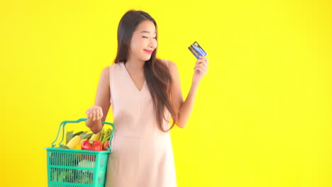Hübsche-Asiatische-Frau-Mit-Korb-Voller-Gemüse,-Die-Kreditkarte-Mit-Einem-Lächeln-Zeigt