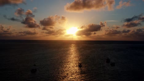 Beautiful-aerial-drone-shot-of-an-ocean-sunrise-at-Well-Beach-near-Joao-Pessoa-on-a-warm-summer-morning-with-the-water-below,-golden-clouds-on-the-skyline,-and-small-boats-in-the-water