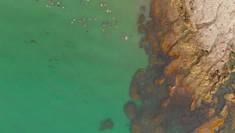 Top-down-aerial-of-rocky-coastline-and-swimmers-in-La-Union,-Philippines