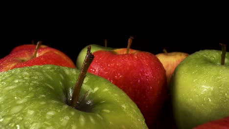 Vista-Macro-Moviéndose-Hacia-Atrás-Sobre-Manzanas-Rojas-Y-Verdes-Frescas-Sobre-Fondo-Negro,-Fruta-Con-Gotas-De-Agua