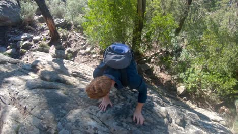 A-slow-motion-shot-of-a-ginger-man-rock-climbing-up-a-small-vertical-boulder-in-the-Australian-bush