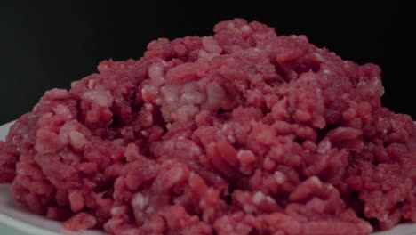 Raw-Ground-Beef-Hamburger-Meat-on-Plate-with-Black-Background,-Pan-Left