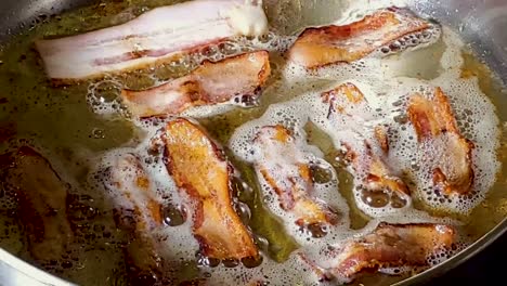 Close-Up-Of-A-Slice-Of-Bacon-Added-To-Fried-Bacon-On-Pan