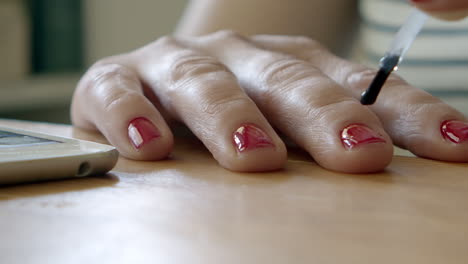 Brushing-lacquer-top-coat-on-red-polish-fingernails-on-table,-macro