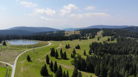 Forest-trails-in-Rogla-sports-resort-Slovenia-during-springtime-passing-around-a-lake,-Aerial-flyover-shot
