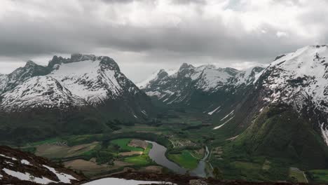 Time-Lapse-of-amazing-scenic-view-of-small-village-in-a-valley,-clouds-passing-over-snowy-mountain-tops