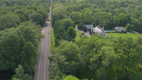 Cars-travel-up-and-down-a-road-and-past-a-nice-house-in-Ladue,-aerial-view