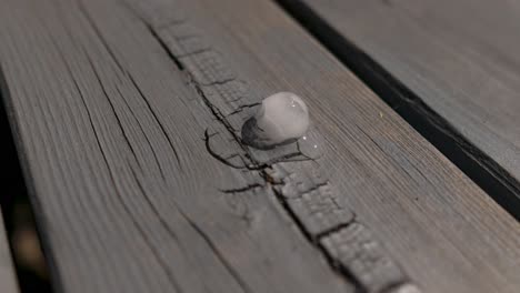 Time-lapse-of-an-ice-cube-melting-on-wooden-table,-laying-in-the-sun