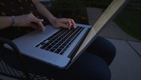 Closeup-of-woman's-hands-using-a-laptop-outside-on-her-driveway-on-a-summer-evening