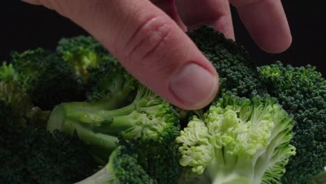 Hand-Takes-Broccoli-Piece-from-Pile,-Close-Up-on-Black-Background