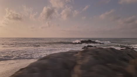 Rocky-dramatic-splashing-waves-on-sunset-coastal-beach-skyline-dolly-flying-right