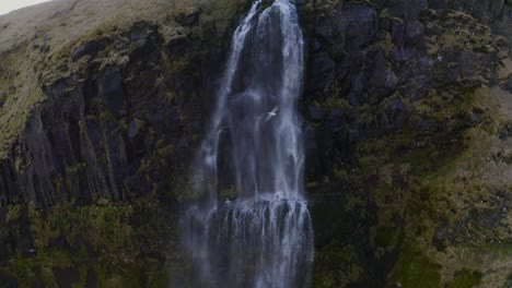 Tilting-down-from-the-top-of-a-tall-waterfall-where-water-is-plummeting-over-the-edge-to-the-ground-far-below