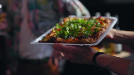 Close-up-shot-of-a-german-baker-holding-a-fresh-baked-flat-bread-pizza-with-arugula-tomatoes-and-bread-salad-stone-oven-and-gives-it-to-guest-25-fps-slowmotion