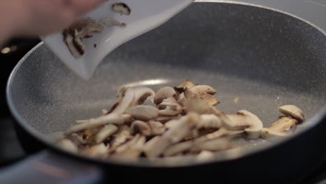 Female-chef-pours-sliced-mushrooms-in-a-frying-pan