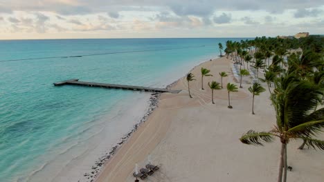 AERIAL-Tropical-Beach-With-Palm-Trees,-Wooden-Jetty-And-Sea-Horizon