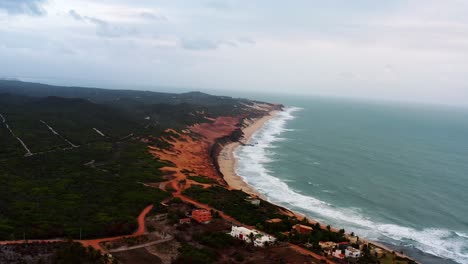 Wide-aerial-drone-shot-of-the-small-hidden-beach-town-of-Sibauma-near-Pipa-in-Northern-Brazil-with-tropical-bright-orange-sand-beaches-and-sandy-roads