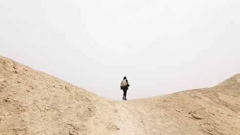 Traveler-woman-walking-through-the-valley,-arid-desert,-misty-atmosphere,-Israel,-traveling-shot